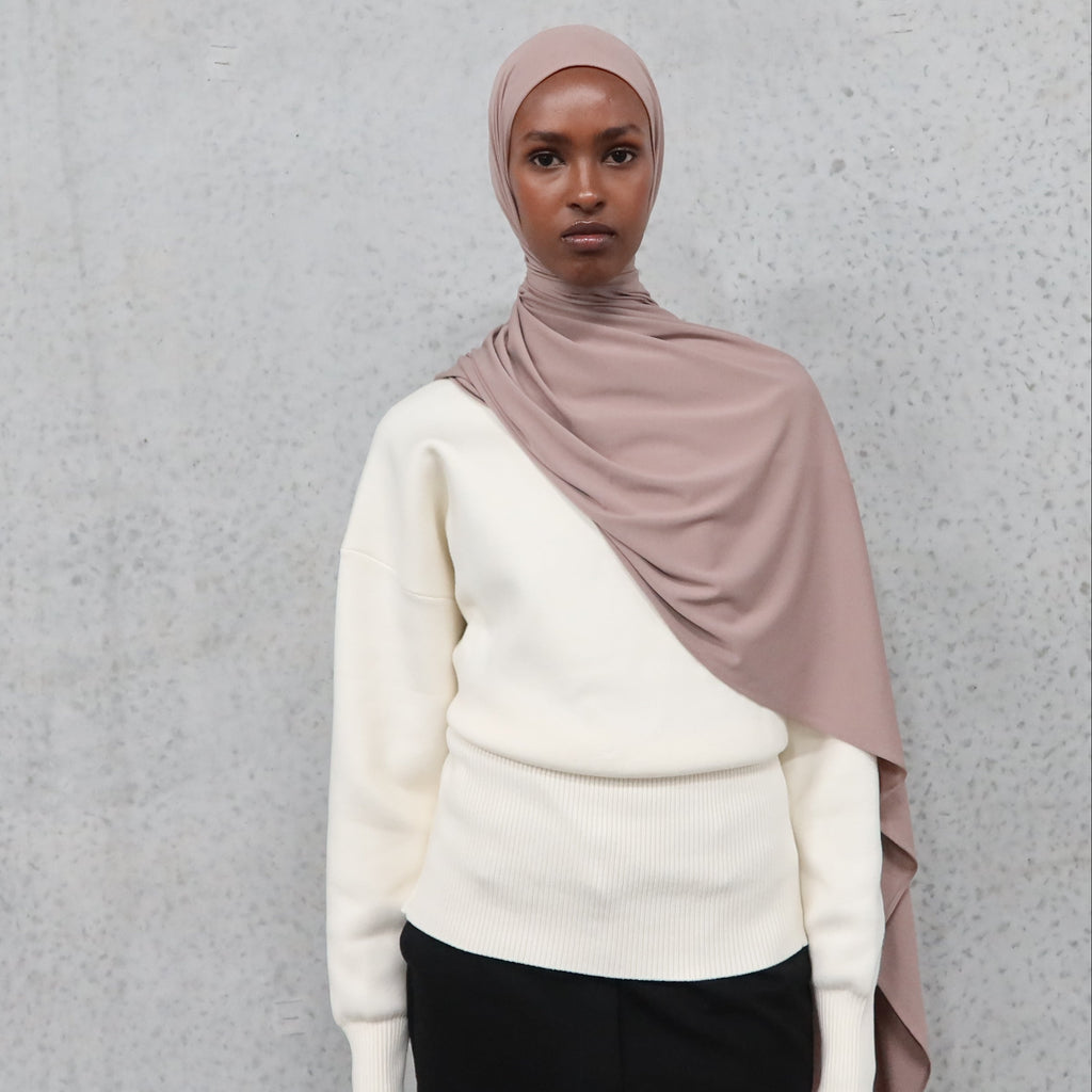 Person wearing a beige hijab and white sweater against a gray background