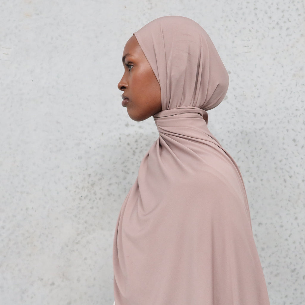Woman wearing a beige hijab against a light gray background